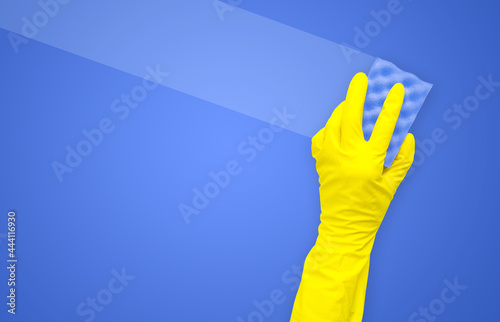 Hand in a yellow rubber glove with a blue cleaning sponge leaves a clean stripe on a blue background with a copy space