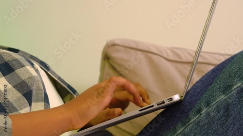 Close-up of a young black womans hand typing on a laptop. The concept of working online while lying on the couch at home. No face.
