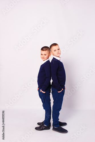 Two boys in dark blue school uniform stand in full height against a white background