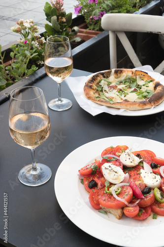 Italian caprese salad with tomatoes  mozzarella  oregano  thassos  onions  chili and olive oil. pizza with roccula and parmesan bacon. two glasses of wine rose in a restaurant on the street