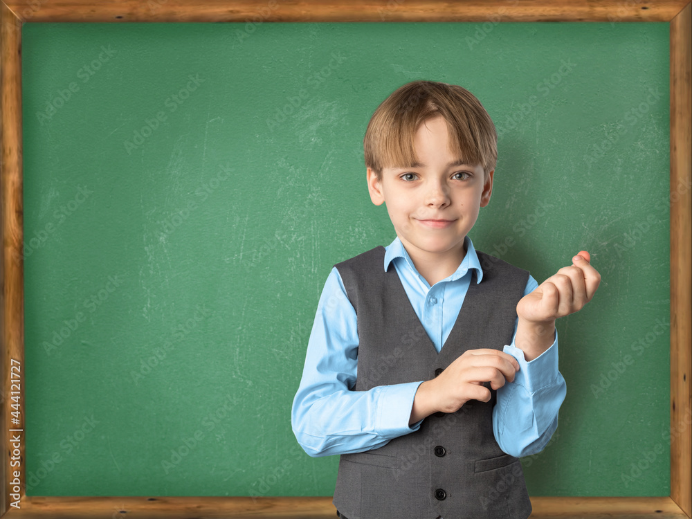 Concept Back to School. A Caucasian boy pupil in front of the classroom board in a school uniform prepares to answer a lesson. The child buttons the button on the shirt Concept Back to School. A Caucasian boy pupil in front of the classroom board in a school uniform prepares to answer a lesson. The child buttons the button on the shirt