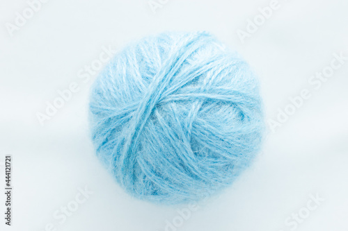 One round ball of blue color in the center of the frame on a white woven background on the theme of hand-made hobby knitting