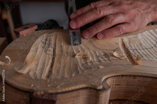Luthier's hands using gouge to work the wood and make a violin