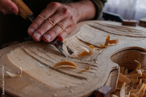 Luthier's hands using gouge to work the wood and make a violin