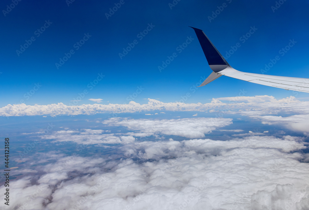 Fototapeta premium Airplane wing view out of the window on the cloudy sky the earth background