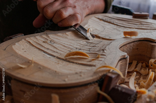 Luthier's hands using gouge to work the wood and make a violin