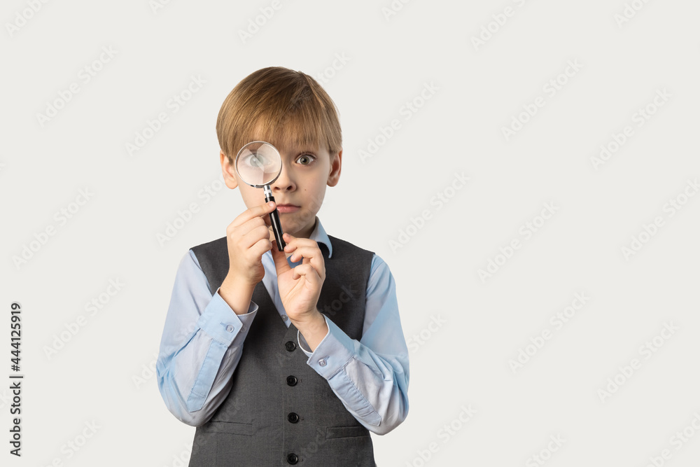 Caucasian boy in school uniform with a magnifying glass in front of his face. A large portrait of a schoolboy on a white background. Concept Back to School Caucasian boy in school uniform with a magnifying glass in front of his face. A large portrait of a schoolboy on a white background. Concept Back to School