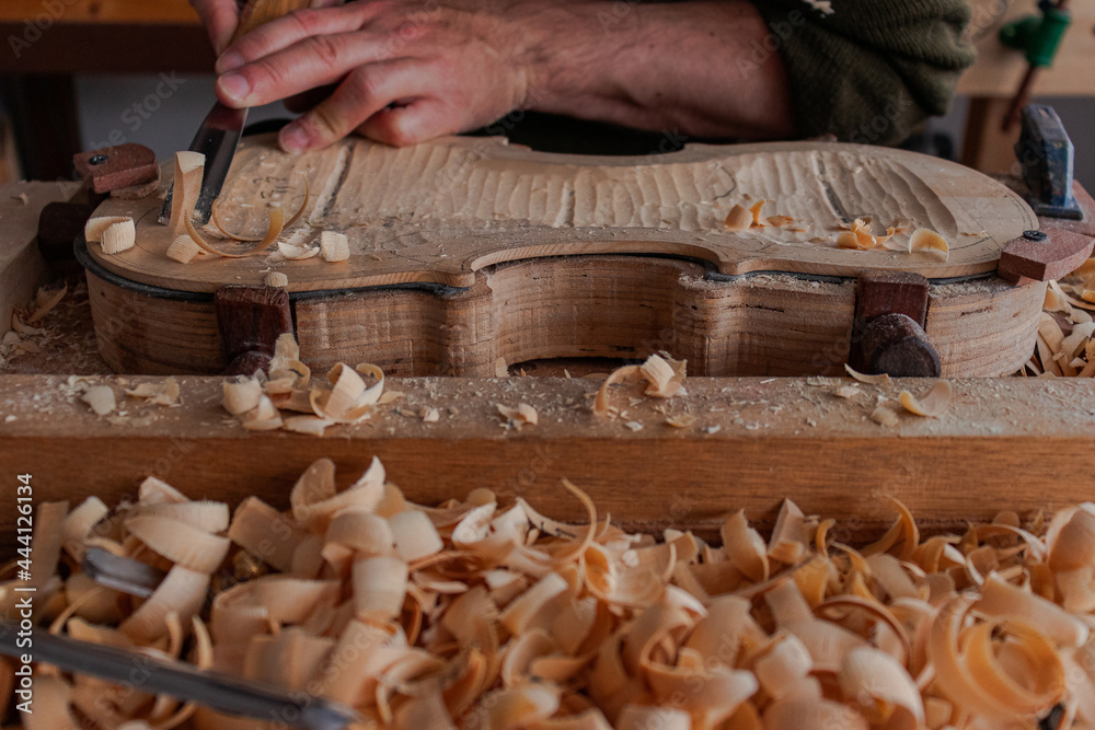 Luthier's hands using gouge to work the wood and make a violin Luthier's hands using gouge to work the wood and make a violin