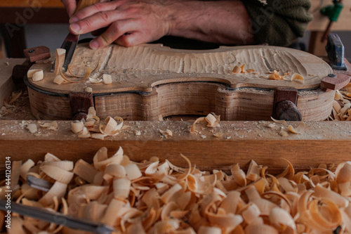 Luthier's hands using gouge to work the wood and make a violin