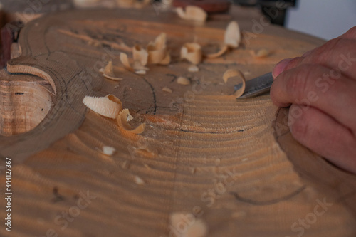 Luthier's hands using gouge to work the wood and make a violin