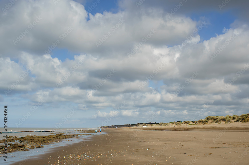 Landscape of a beach with some people walking and wide blue sky with white cotton clouds Landscape of a beach with some people walking and wide blue sky with white cotton clouds
