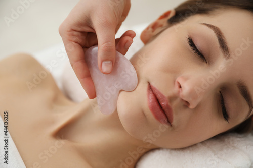Young woman receiving facial massage with gua sha tool in beauty salon, closeup photo