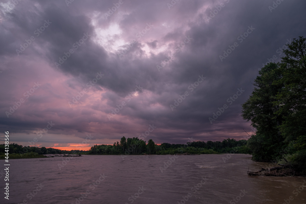 a purple cloud at sunset is reflected in the river