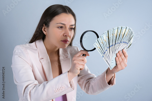 Expert authenticating 100 dollar banknotes with magnifying glass on light grey background. Fake money concept photo