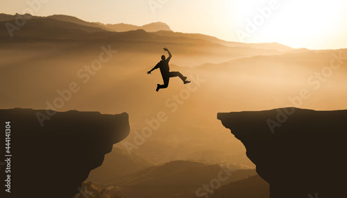 Silhouette jumping cliff sunset mountain. Courageous Man Jump Between Two Cliffs. Business Goals achievement concept 