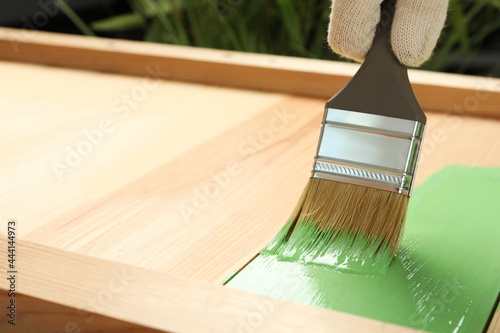 Fototapeta Naklejka Na Ścianę i Meble -  Worker applying green paint onto wooden surface, closeup. Space for text