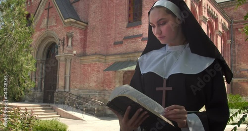 Young nun reading Bible outdoors near monastery