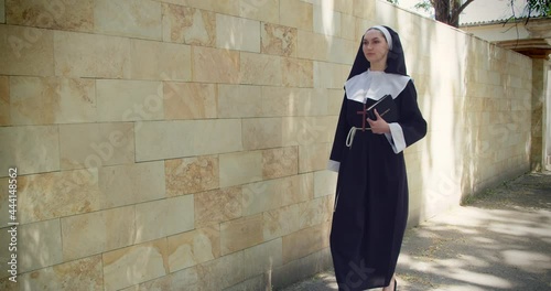 Young nun with Bible walking outdoors