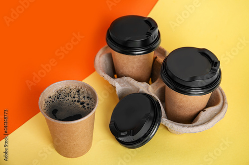 Takeaway paper coffee cups with plastic lids and cardboard holder on color background