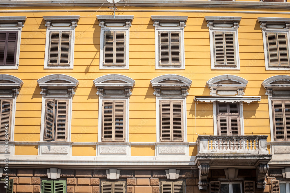 Typical italian mediterranean facade of a residential building, yellow, with traditional European wooden blinds and a balcony, on a vintage old house, in istria region, by the adriatic...