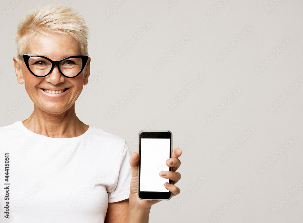 Portrait of a senior smiling woman with short hair wearing glasses showing or presenting mobile phone application. Portrait of a senior smiling woman with short hair wearing glasses showing or presenting mobile phone application.