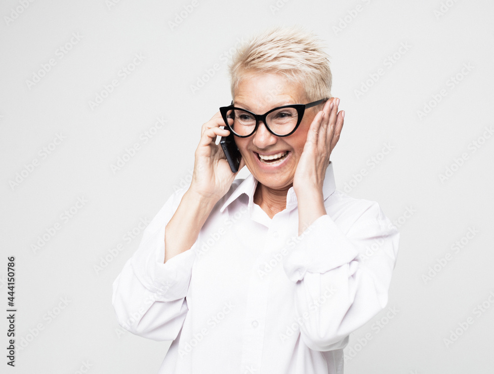 Surprised aged woman using phone, isolated over grey background.