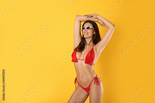 Beautiful woman in stylish bikini and sunglasses on yellow background. Space for text