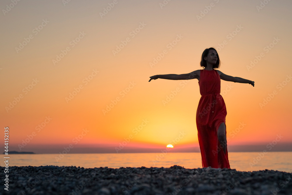 silhouette of a girl at sunset on the background of the sea with outstretched arms
