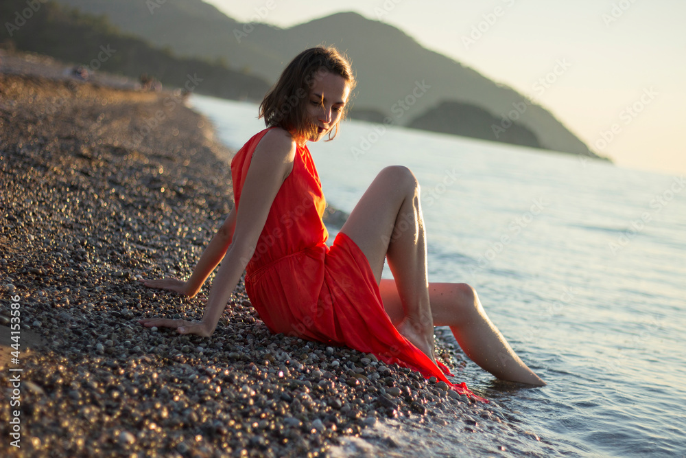 stylish beautiful girl in a red dress sitting and posing at sunset ...