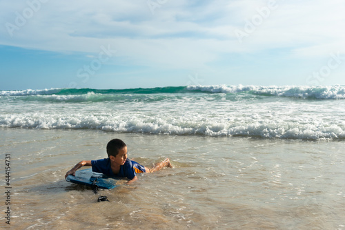 A boy lay down on body board while the wave move to the beach..Paradise beach blue sea, and clear sand landscape. .waves crashing on the beach background..smiling face of happy boy relax concept.