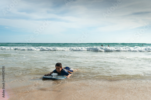 The waves swept the surf boy toward the shore..boy surfing on white waves..Paradise beach blue sea, and clear sand landscape background..smiling face of happy boy surfing concept.