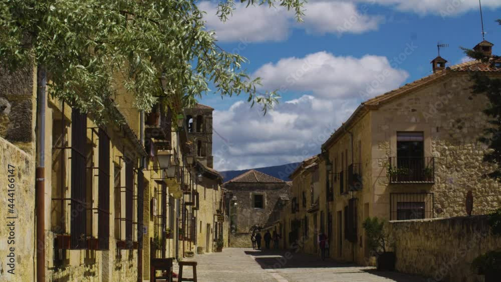 Tourists Walking At The Road Surrounded With Medieval Buildings In Pedraza Town In Segovia, Spain. wide shot Tourists Walking At The Road Surrounded With Medieval Buildings In Pedraza Town In Segovia, Spain. wide shot