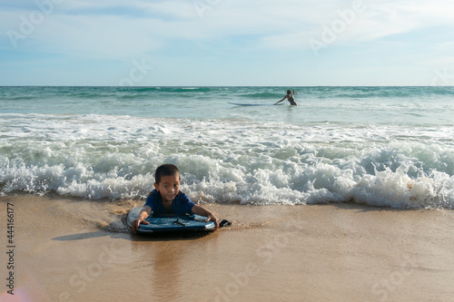 The waves swept the surf boy toward the shore..boy surfing on white waves..Paradise beach blue sea, and clear sand landscape background..smiling face of happy boy surfing concept. © Narong Niemhom