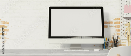 Computer monitor with mock-up screen on the desk with supplies and brick wall background, 3D render