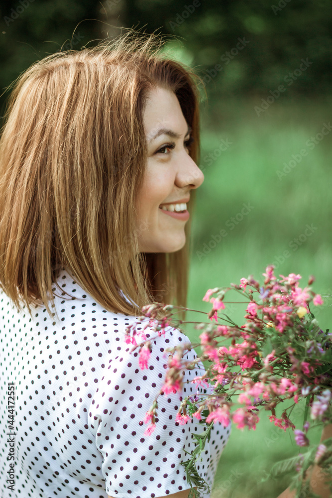 A girl with a short haircut laughs and holds flowers in her hands. A close portrait from the back of a young beautiful woman in a meadow with a bouquet of lilac wildflowers. Selective focus A girl with a short haircut laughs and holds flowers in her hands. A close portrait from the back of a young beautiful woman in a meadow with a bouquet of lilac wildflowers. Selective focus