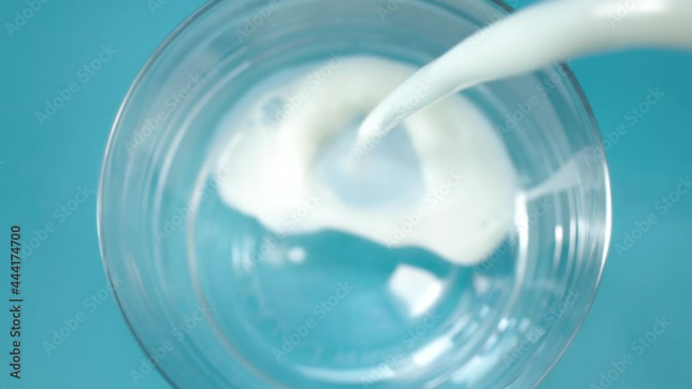 Pouring delicious fresh milk into clean glass standing on light blue table at bright light extreme close view from above slow motion Pouring delicious fresh milk into clean glass standing on light blue table at bright light extreme close view from above slow motion