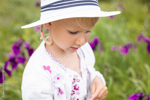 little girl in white hat and dress in field of irises flowers 