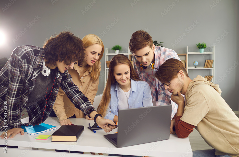 Group of students working on a joint university project sitting at a laptop in the classroom. Boys and girls discuss the learning task. Concept of teamwork, educational projects Group of students working on a joint university project sitting at a laptop in the classroom. Boys and girls discuss the learning task. Concept of teamwork, educational projects