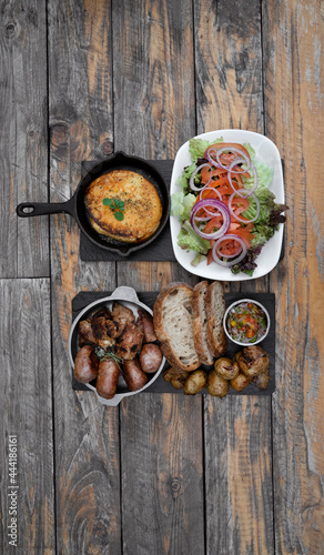 Argentinian traditional food. Top view of a barbecue with chorizos, pork sausages, bread, grilled sweetbreads and provolone cheese, criolla sauce and a fresh salad served on the wooden table. 