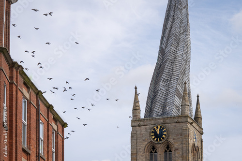 Chesterfield crooked spire church with birds flying in sky. St Marys Church Chesterfield, Derbyshire with twisted steeple spire.