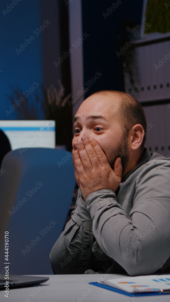 Happy cheerful businessman smiling while looking at laptop computer display receiving online good job promotion. Joyful happy executive manager working in company office late at night