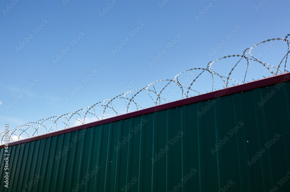Metal wall with barbed wire against the blue sky background. Fence with barbwire for protection, space for text Metal wall with barbed wire against the blue sky background. Fence with barbwire for protection, space for text