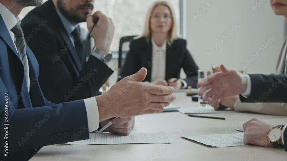 PAN midsection slowmo shot of two businessmen with lawyers sitting by conference table shaking hands and signing papers after making successful deal