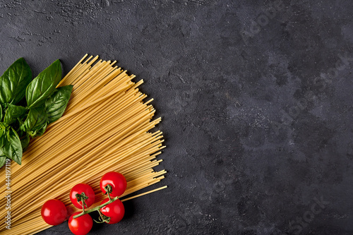 Spaghetti Italian pasta with basil leaves and tomatoes on dark textured background, arranged in the colors of the Italian flag. Top view. Copy space