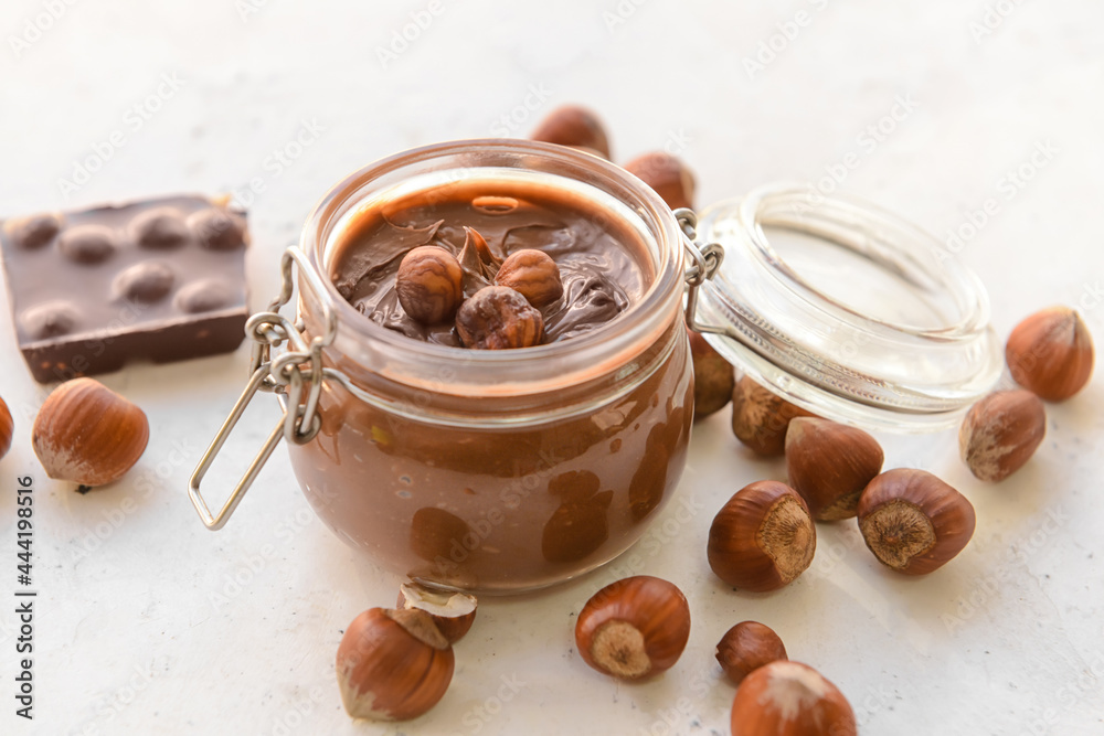 Jar with tasty chocolate paste and hazelnuts on light background Jar with tasty chocolate paste and hazelnuts on light background