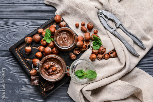 Composition with tasty chocolate paste and hazelnuts on dark wooden background