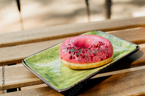 Sweet and colorful pink donut close-up on a green plate. Summer terrace in a cafe