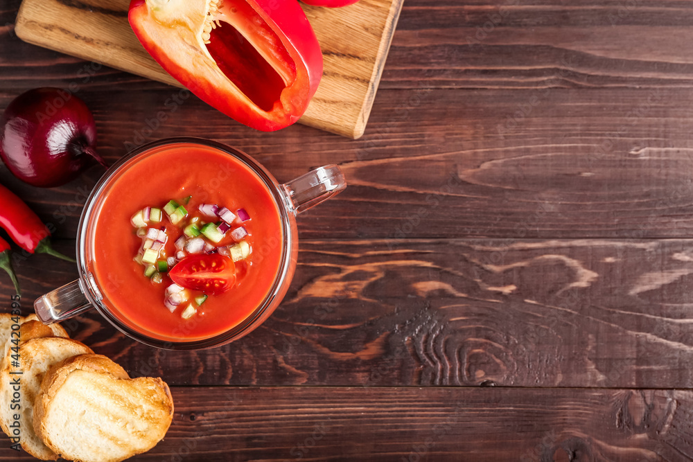 Fototapeta premium Glass pot with tasty gazpacho and bread slices on wooden background
