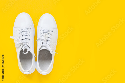 White leather sneakers with laces on yellow background