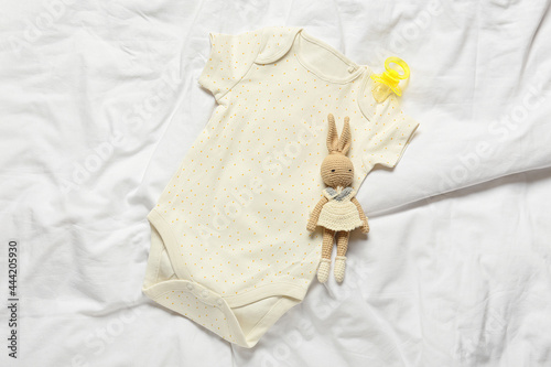 Baby bodysuit, toy and pacifier on bed